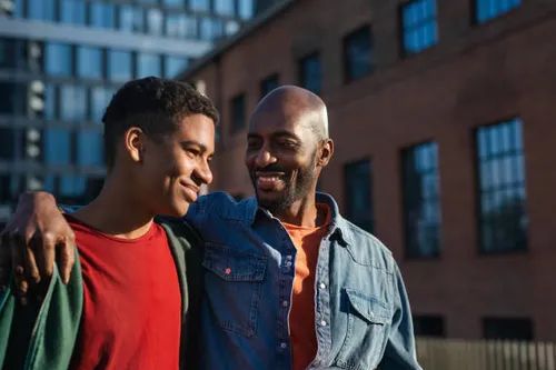 A mentor with his arm around a young man, both smiling outdoors