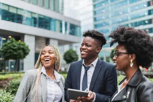 Three young adults smiling and talking together outdoors in the city